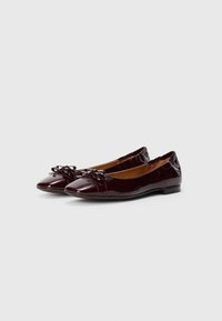 Ballerines en cuir verni bordeaux avec un bout rond, un nœud à l'avant et une semelle plate. Surface lisse et brillante.