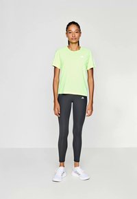 Lichtgroen sportshirt met korte mouwen en ronde hals, gecombineerd met zwarte leggings en witte sneakers. Het shirt heeft een logo.