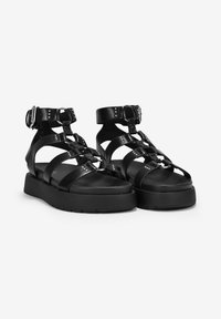 Sandalias negras con tiras, suela gruesa, cierre de hebilla, diseño plano y acentos metálicos en las tiras.