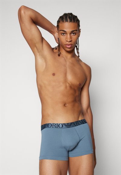 Kék pamut boxeralsó fekete rugalmas derékszíjjal, melyen "Emporio Armani" márkajelzés található. Sima textúra, testhezálló dizájn és rövid láb kivágás.