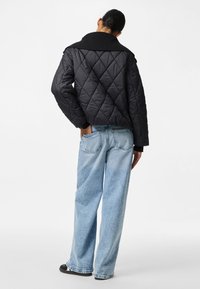 Must kolmnurkse krae ja musta värvi kviltjakki, mille juurde on sobitatud helesinised laiad püksid ja mustad jalanõud. Tekstuuriline, lõdva istuvusega.