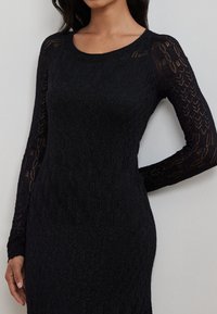 Czarna dzianinowa sukienka z długimi rękawami, z teksturowanym wzorem oraz okrągłym dekoltem. Gładka tekstura z delikatnym połyskiem.