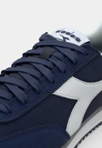Marineblå sneakers med mesh-overdel, suede-detaljer, hvit logo og flate snører. Strukturert såle med en kontrastfarge på yttersålen.