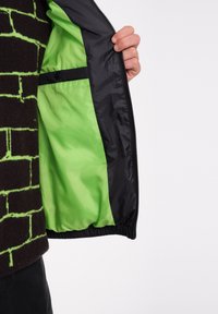 Zwarte buitenjas met een felgroene binnenvoering, voorzien van een rits en elastische manchetten. Inclusief interne zakken.