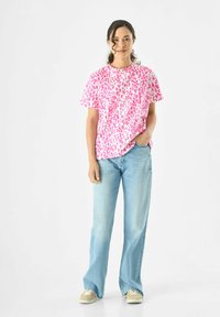 Roze luipaardprint t-shirt gecombineerd met lichtblauwe wijde jeans en beige sneakers. Het t-shirt heeft korte mouwen en een ontspannen pasvorm.