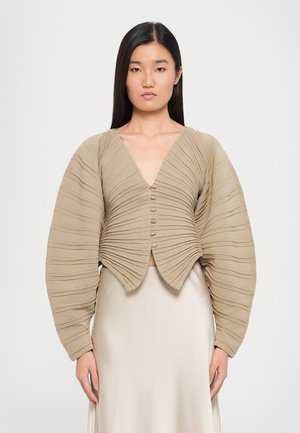 Top court beige avec texture côtelée, décolleté en V profond et manches bouffantes. Comprend six boutons sur le devant. Tissu lisse en bas.