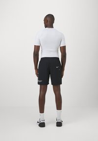 Valkoinen lyhythihainen urheilupaita, yhdistettynä mustiin shortseihin, joissa on sivutaskut ja Nike-logo, neutraalin taustan edessä.