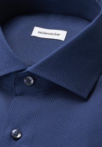 Marineblauw shirt van een gestructureerde stof, met een traditionele kraag en knoopsluiting, voorzien van een "seidensticker" label.