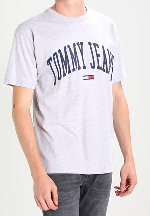 Szary bawełniany t-shirt z okrągłym dekoltem, z napisem „TOMMY JEANS” w granatowych łukach oraz małym czerwono-białym logo pod spodem.