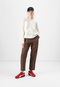 Vit stickad tröja med ett strukturerat mönster, bruna vida byxor och röda sneakers med vita accenter, tillsammans med en svart keps.