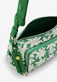 Borsa in tessuto con motivo floreale verde, chiusura con zip, tracolla verde staccabile e un'etichetta con la scritta "I ❤️ Desigual." Superficie testurizzata.