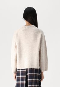 Ανοιχτό μπεζ, υφασμάτινο πουλόβερ με στρογγυλή λαιμόκοψη και χαμηλούς ώμους. Διαθέτει ριμπ μανσέτες και τελείωμα. Συνδυάζεται με μια καρό φούστα.