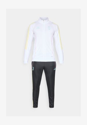 Bijela trenirka s lijepim žutim i ružičastim detaljima. Jakna ima patentni zatvarač sprijeda i visok ovratnik. Crne hlače s odgovarajućim logotipima i prugama.