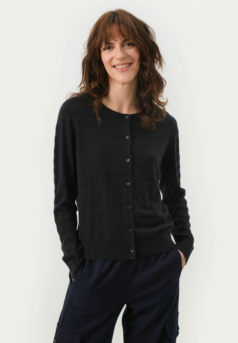 Cardigan negru dintr-un material moale, cu un decolteu rotund, închidere cu butoane și mâneci lungi, asortat cu pantaloni negri.