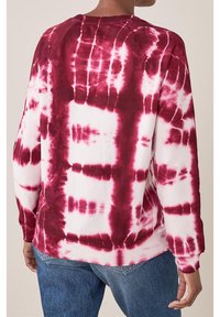 Felpa a maniche lunghe in tie-dye bianco e rosso scuro. Presenta un collo e un orlo a coste con un motivo testurizzato. Vestibilità ampia.