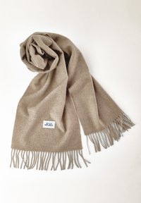 Beige Wollschal mit Fransen, zu einem Spiralroll gewickelt. Verfügt über ein kleines weißes Etikett mit dem Schriftzug "STYLE REPUBLIC". Weiche Textur.