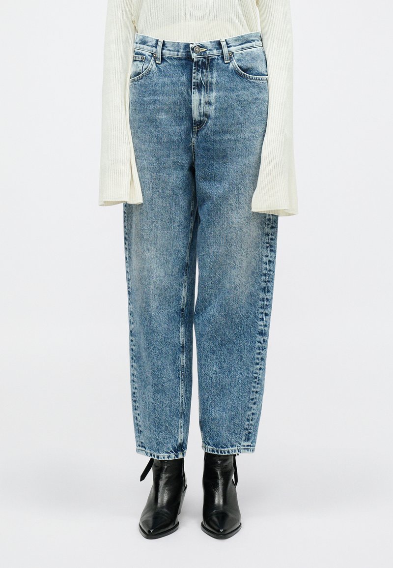 Ανοιχτό μπλε ψηλόμεσα τζιν παντελόνια με χαλαρή εφαρμογ�ή και ξεθωριασμένο φινίρισμα, διαθέτοντας μπροστινές τσέπες και κλείσιμο με κουμπί, συνδυασμένα με μαύρες μποτάκια ως τον αστράγαλο.