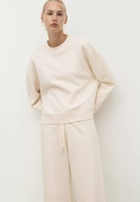 Sweatshirt beige clair avec un col rond, des épaules tombantes et des poignets en côtes. Associé à un pantalon de survêtement fuselé assorti avec un cordon de serrage.