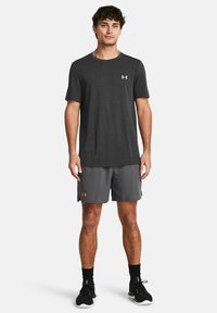 Camiseta atlética gris con cuello redondo y una textura sutil, combinada con pantalones cortos gris que presentan un logo naranja. Zapatillas deportivas negras.