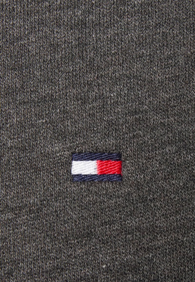 Tissu tricoté gris avec un petit logo rectangulaire présentant des bandes horizontales en blanc, rouge et bleu marine.