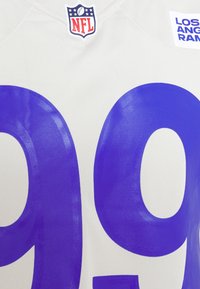 Koszulka NFL Los Angeles Rams w jasnoszarym kolorze z dużymi fioletowymi cyframi "99" wyraźnie widocznymi. Posiada logo NFL przy kołnierzyku.