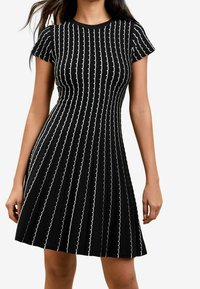 Czarna sukienka z krótkimi rękawami, ozdobiona białymi poziomymi falistymi liniami oraz rozkloszowanym dołem. Tkanina o fakturze.