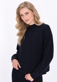 Marineblauer gerippter Pullover mit hohem Kragen, weiten Ärmeln und lockerer Passform, der dezente Nahtdetails an der Vorderseite aufweist.