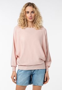 Helles rosa, locker sitzendes Sweatshirt mit langen, gerafften Ärmeln aus einem weichen, strukturierten Stoff, kombiniert mit Jeansshorts.