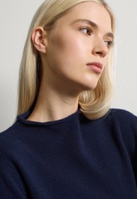 Suéter de punto azul marino con un cuello alto y una textura suave. Vista cercana del material y detalle del cuello.