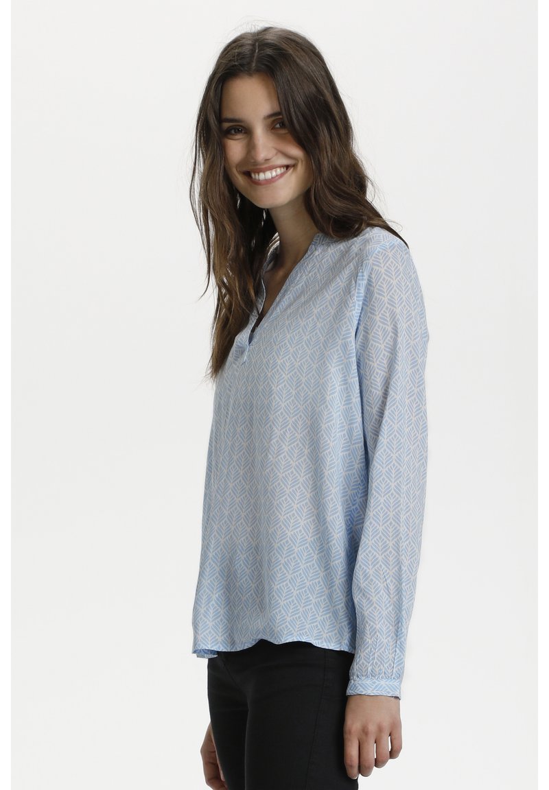 Blouse bleu clair avec un motif géométrique de feuilles, manches longues, encolure en V et ourlet légèrement arrondi, fabriquée à partir d'un tissu léger.