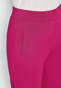 Aangeklede roze broek met een gladde textuur, voorzien van een brede tailleband en een zijzak. De stof heeft een lichte glans.