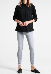 Black button-up shirt with a collar and rolled 3/4 sleeves, paired with light gray skinny jeans and black loafers with a buckle detail.