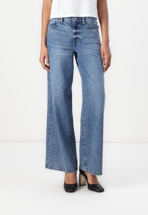 Hellblaue weit geschnittene Jeans aus Denim mit einem verwaschenen Finish, ausgestattet mit einem Knopfverschluss und fünf Taschen. Kombiniert mit schwarzen Schuhen mit Absatz.