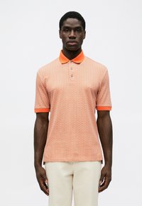 Cămașă polo cu mânecă scurtă, de culoare portocalie, având un model geometric, cu un guler contrastant și închidere cu trei nasturi. Confecționată dintr-un material texturat.
