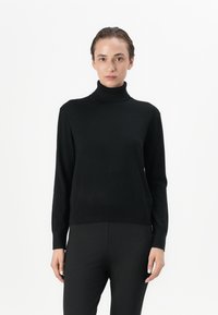 Black turtleneck sweater made of soft material with long sleeves and a fitted design, paired with black tapered pants.