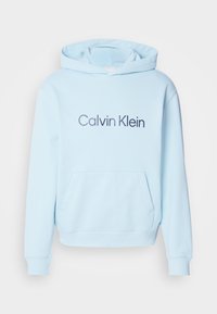 Svetlomodrá mikina s kapucňou vyrobená z mäkkej látky, ktorá má predné vrecko a výrazné logo "Calvin Klein" vytlačené tmavomodrou farbou.