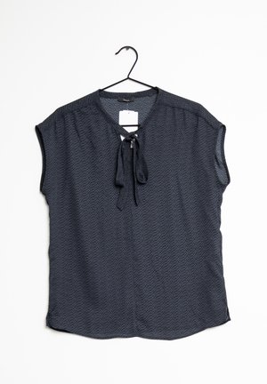 Donkerblauwe blouse met korte mouwen en subtiel patroon, ronde hals, strikdetail en label, hangend aan een zwarte hanger tegen een witte achtergrond.