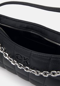 Borsa a tracolla in pelle nera trapuntata con un accento in catena argentata. Presenta un interno con zip e un logo impresso. Forma compatta e rettangolare.