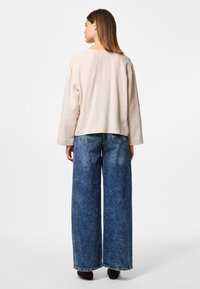 Light beige textured long-sleeve top with a relaxed fit, paired with wide-leg blue denim jeans, featuring rear pockets and a faded finish.
