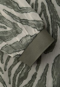 Manchette en tissu gris clair avec des motifs abstraits ondulés gris foncé, dotée d'un poignet en maille côtelée de couleur olive unie.