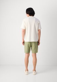Lysfarvet t-shirt med et struktureret mønster, parret med grønne shorts. Modellen har beige sneakers på. Neutral baggrund.