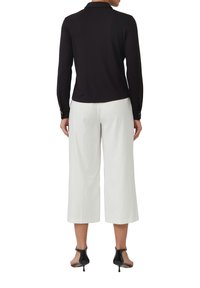 Zwarte lange mouw polo met kraag, gecombineerd met witte brede broek. Zwarte hakken met banden maken de outfit compleet. Glad stoftextuur.