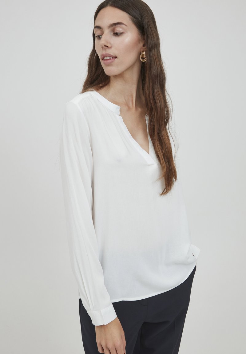 Witte blouse met lange mouwen van een lichtgewicht stof, met een V-hals en geplooide achterkant, gecombineerd met een donkere broek. Eenvoudig, elegant ontwerp.