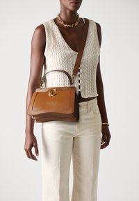 Brown leather handbag with a structured design, featuring a gold hardware clasp, short handle, and an adjustable shoulder strap.