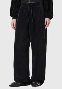 Svarta sammet bredbenade byxor med elastisk midja och dragsko. Slät textur och avslappnad passform, i kombination med platta skor.