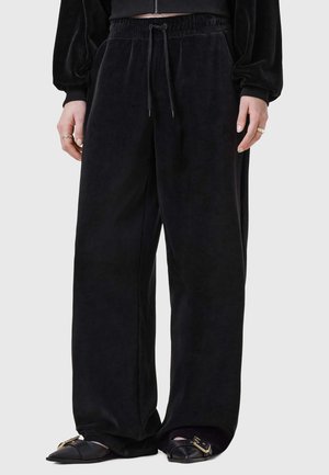 Zwarte fluwelen wijde broek met een elastische tailleband en trekkoord. Gladde textuur en ontspannen pasvorm, gecombineerd met platte schoenen.