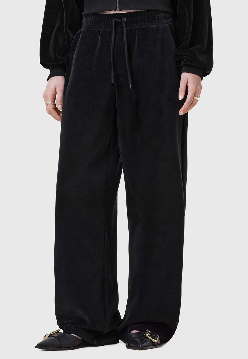 Svarta sammet bredbenade byxor med elastisk midja och dragsko. Slät textur och avslappnad passform, i kombination med platta skor.