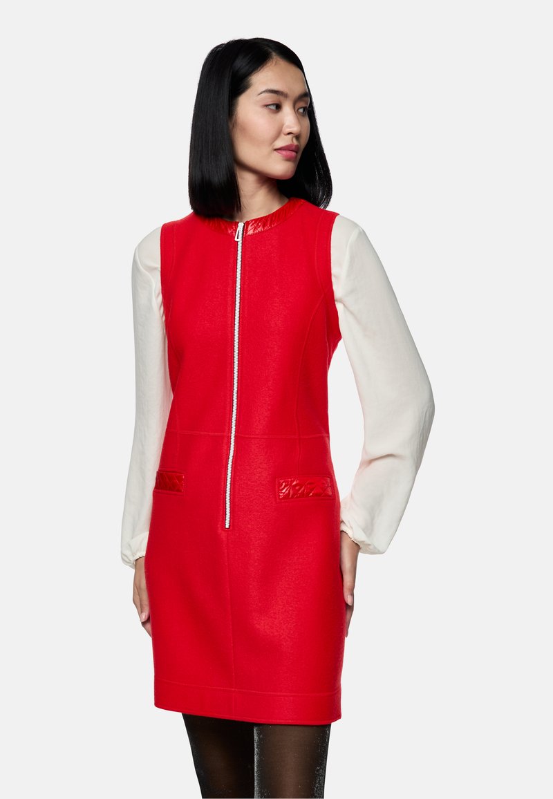 Rotes ärmelloses Kleid mit hohem Kragen und Frontreißverschluss. Kontrastierende weiße lange Ärmel, strukturierte Taschen und glänzende Akzente.