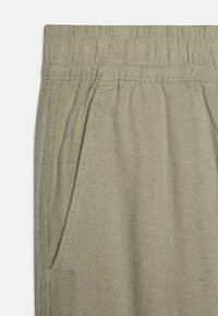 Pantaloni in lino di un verde tenue con vita elasticizzata, tasche laterali e una superficie testurizzata. Design semplice e funzionale.