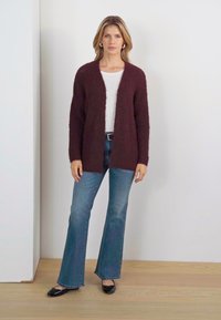 Burgundy knit cardigan with an open front, long sleeves, and a textured finish, paired with light blue flared jeans and black flats.